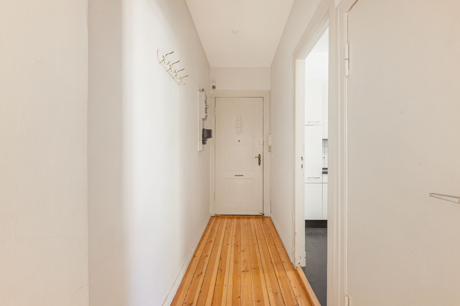 Heller Flur mit Holzboden, Garderobenhaken an der Wand und einer weißen Eingangstür.