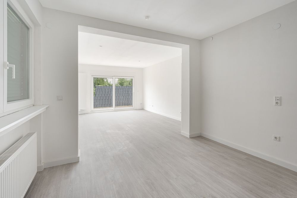 Leerer, heller Wohnraum mit großen Fenstern und Tür zum Garten.