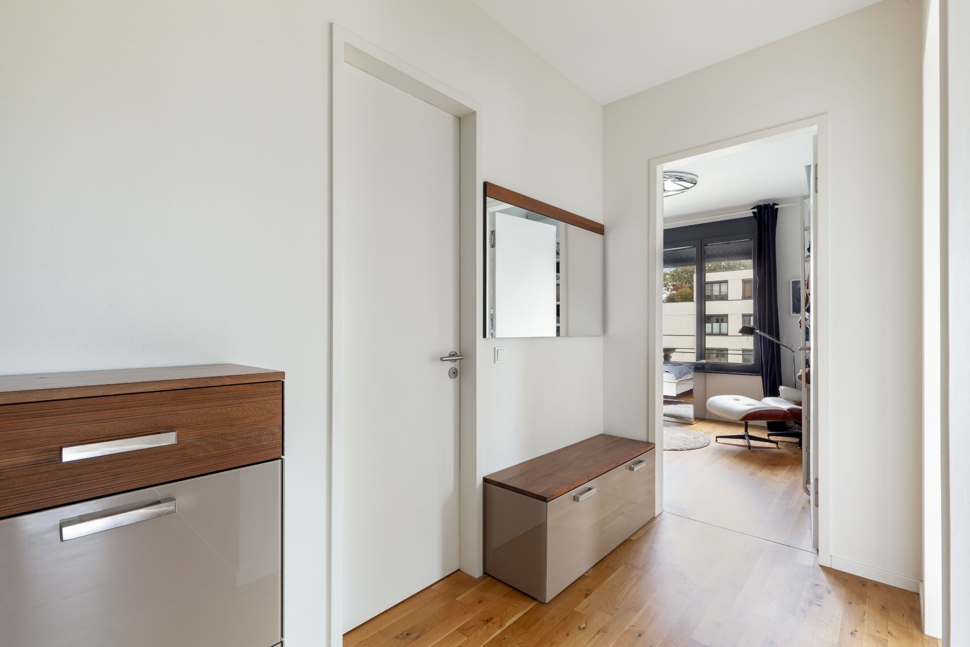 Heller Flur mit Holzfußboden, Spiegel, Kommode und Blick in ein Wohnzimmer.