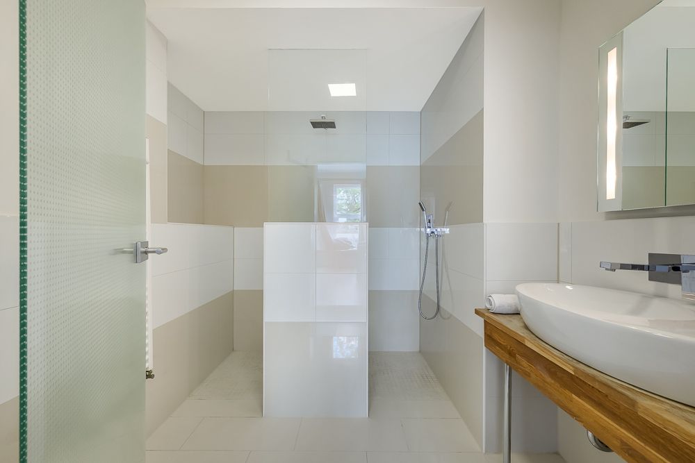 Modernes Badezimmer mit begehbarer Dusche, Waschbecken auf Holzplatte und beleuchtetem Spiegel.