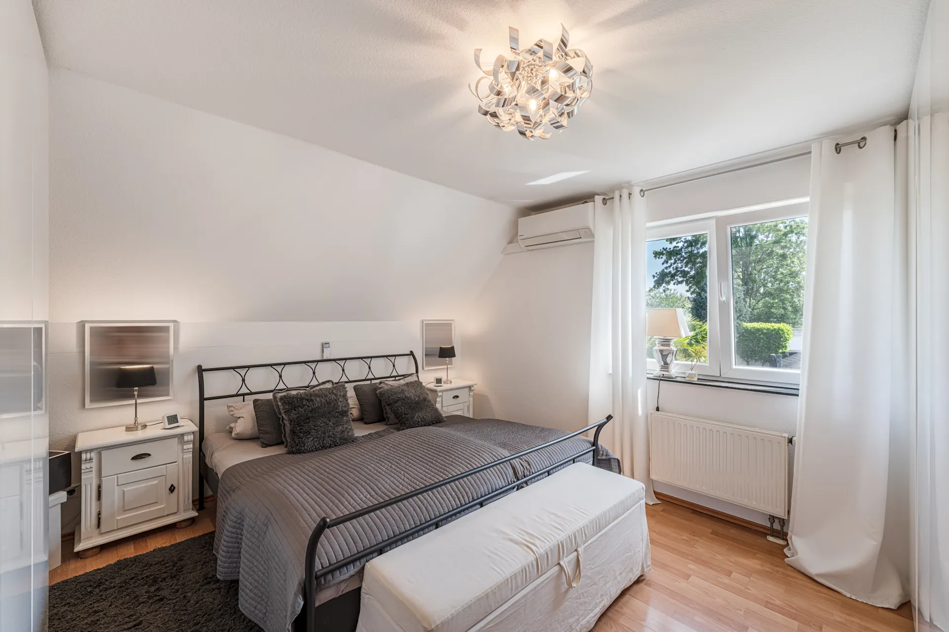 Helles Schlafzimmer mit großem Bett, Nachttischen, Lampe, Fenster und Vorhängen.