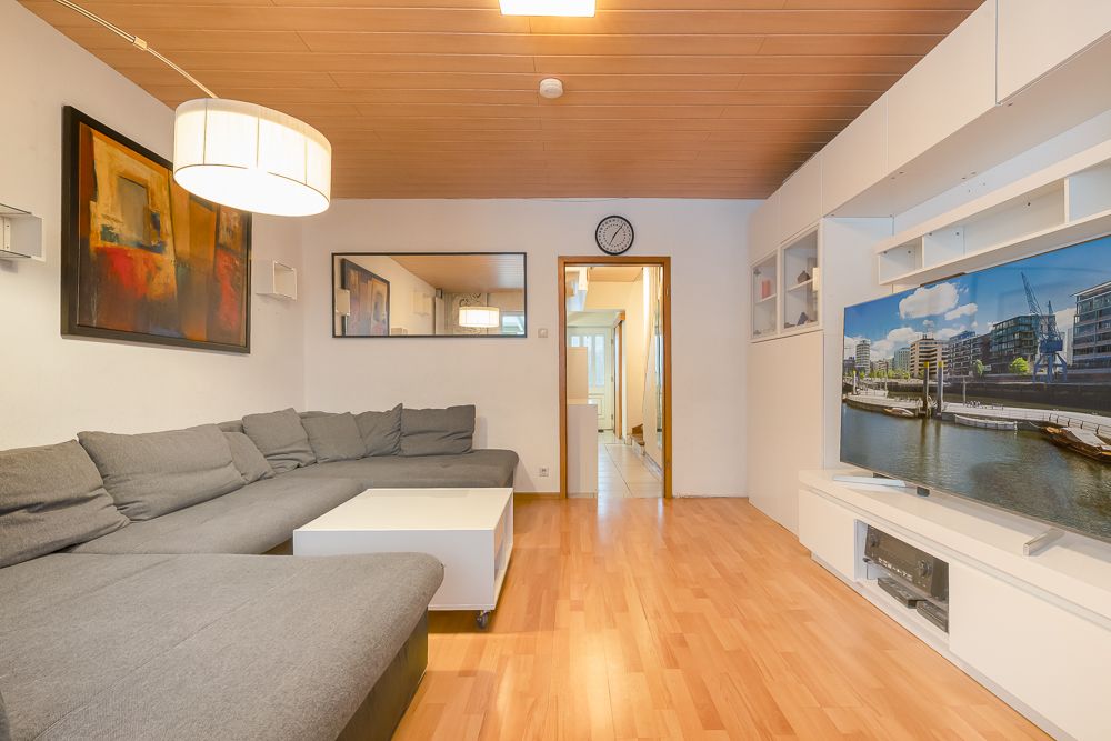 Wohnzimmer mit grauem Ecksofa, Couchtisch, Fernseher und Wandbildern auf Parkettboden.