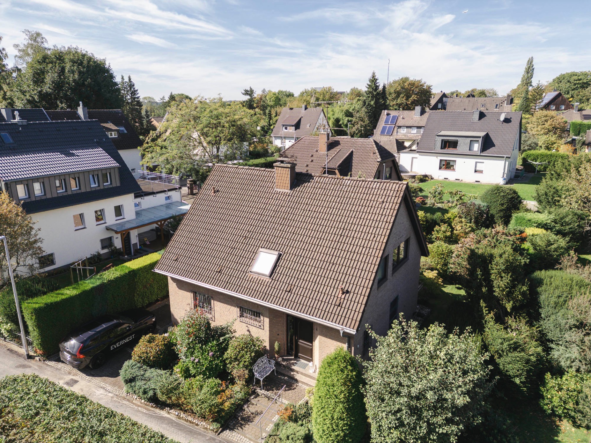Einfamilienhaus mit Garten, umgeben von weiteren Häusern und viel Grün.