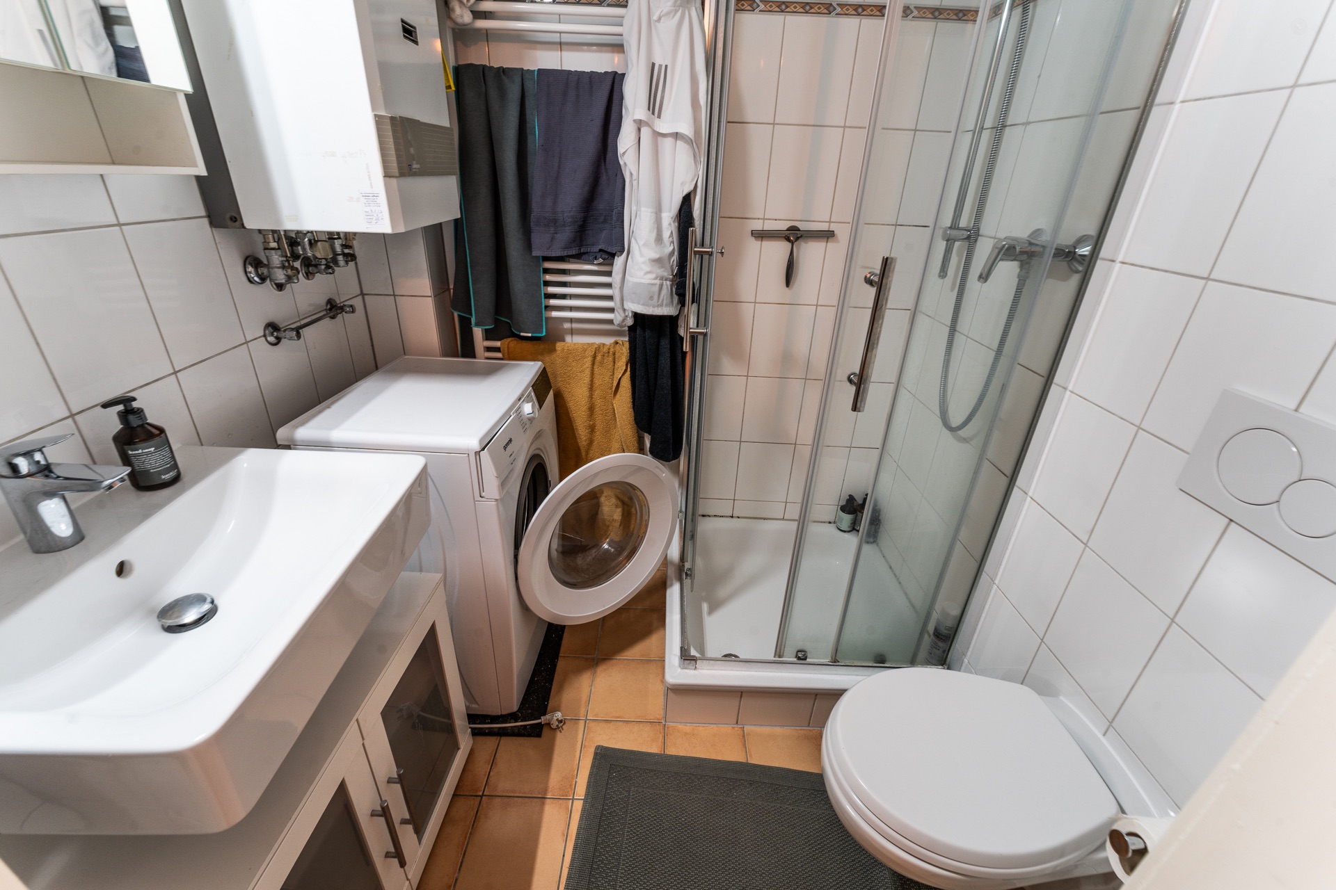 Kleines Badezimmer mit Waschmaschine, Waschbecken, Dusche und Toilette.