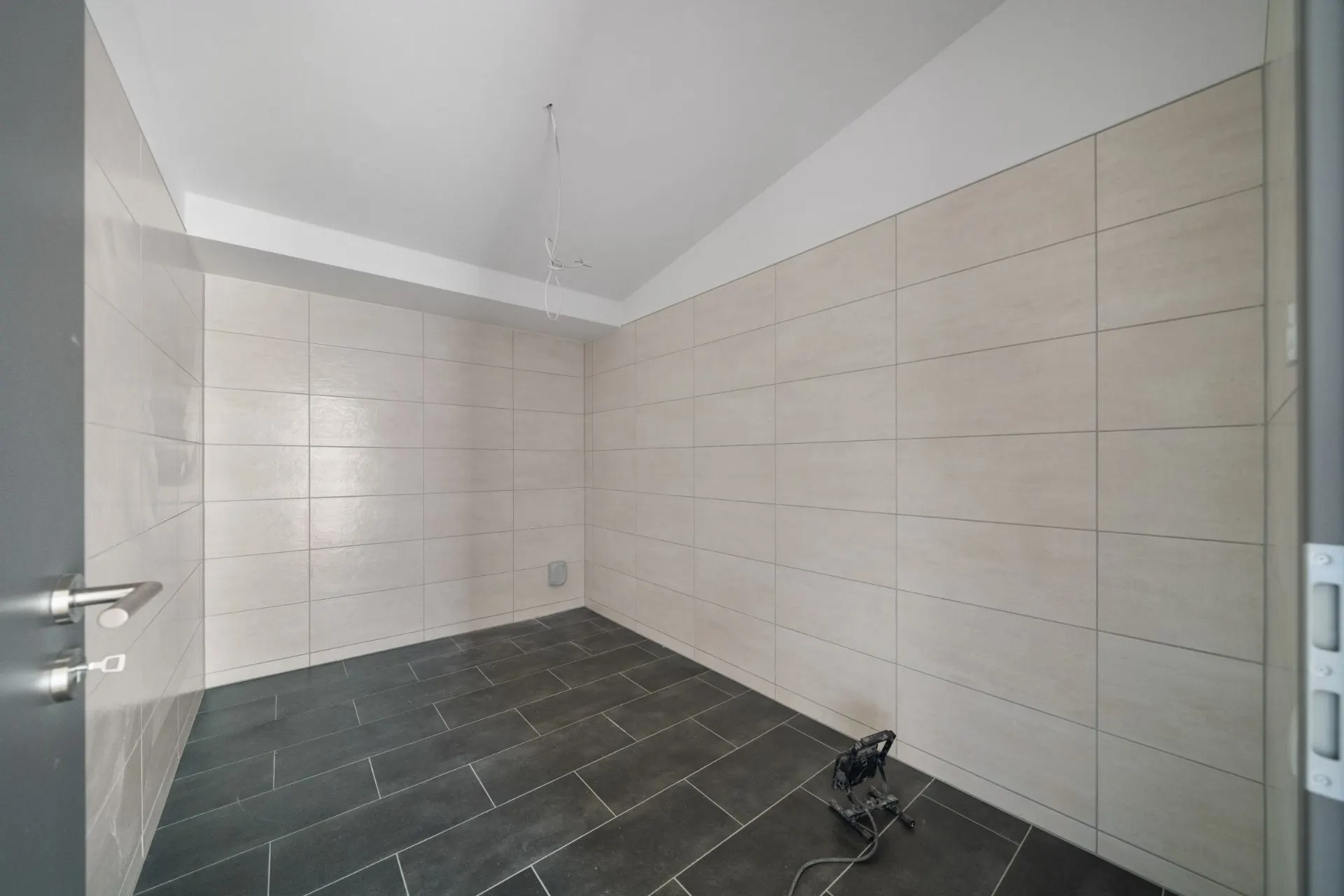 Leerer Raum mit beigefarbenen Wandfliesen und dunklem Bodenfliesen.