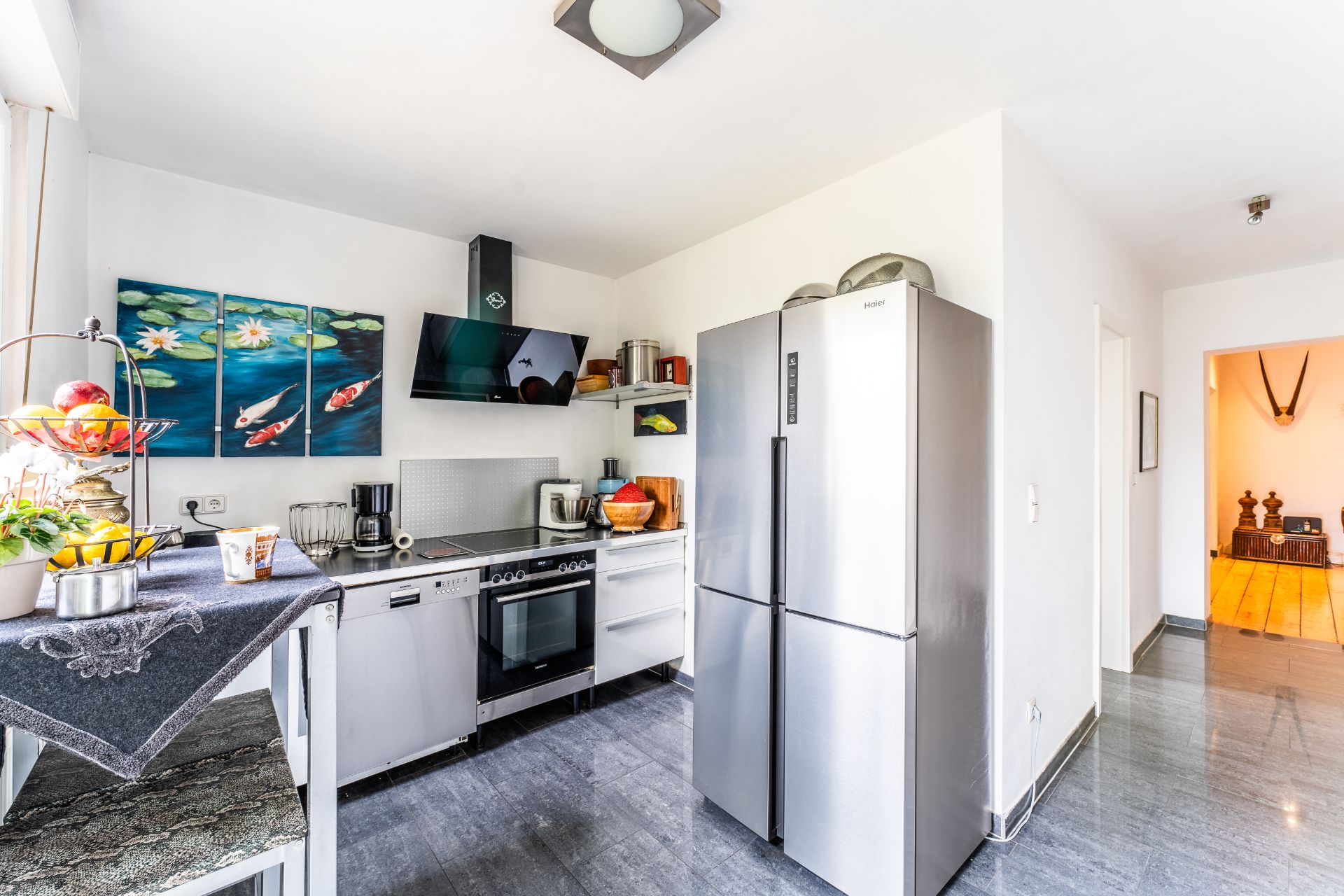 Moderne Küche mit großem Kühlschrank, Herd, Geschirrspüler und farbigem Wandbild mit Fischen.