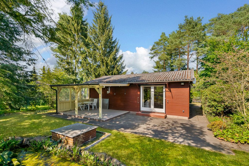 Gemütliches Haus mit Terrasse, Gartentisch und Stühlen, umgeben von Bäumen und Rasen.