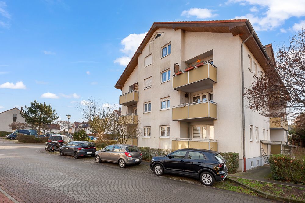 Mehrfamilienhaus mit mehreren Balkonen und geparkten Autos davor bei Tag.
