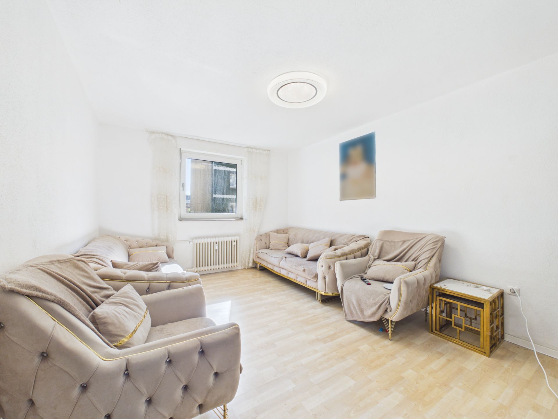 Helles Wohnzimmer mit drei beigen Sofas, Fenster und kleinem Beistelltisch.