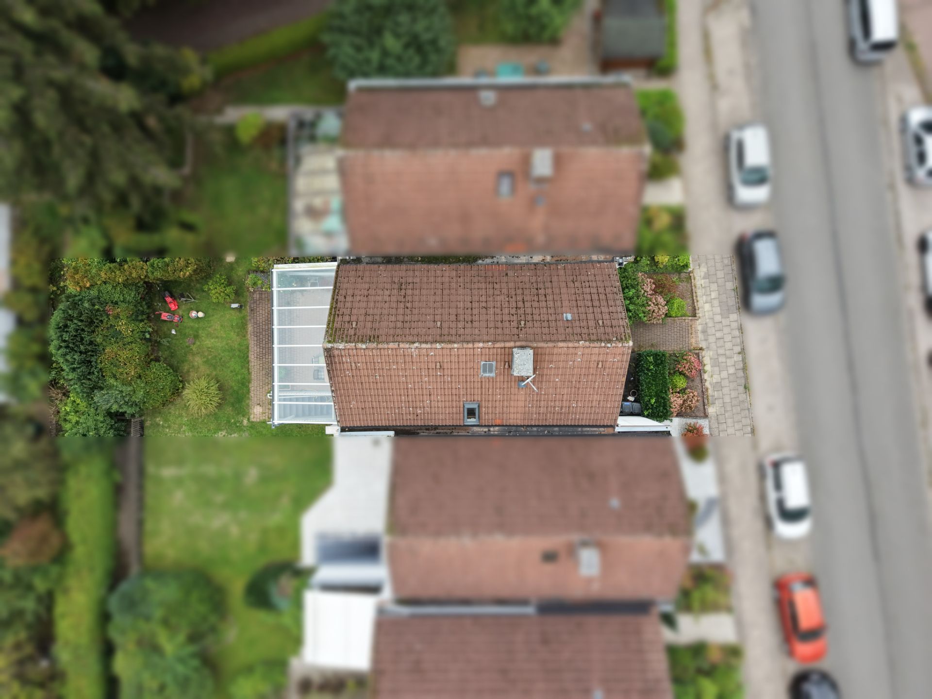 Luftaufnahme eines Einfamilienhauses mit Garten und Wintergarten, umgeben von Nachbarhäusern.