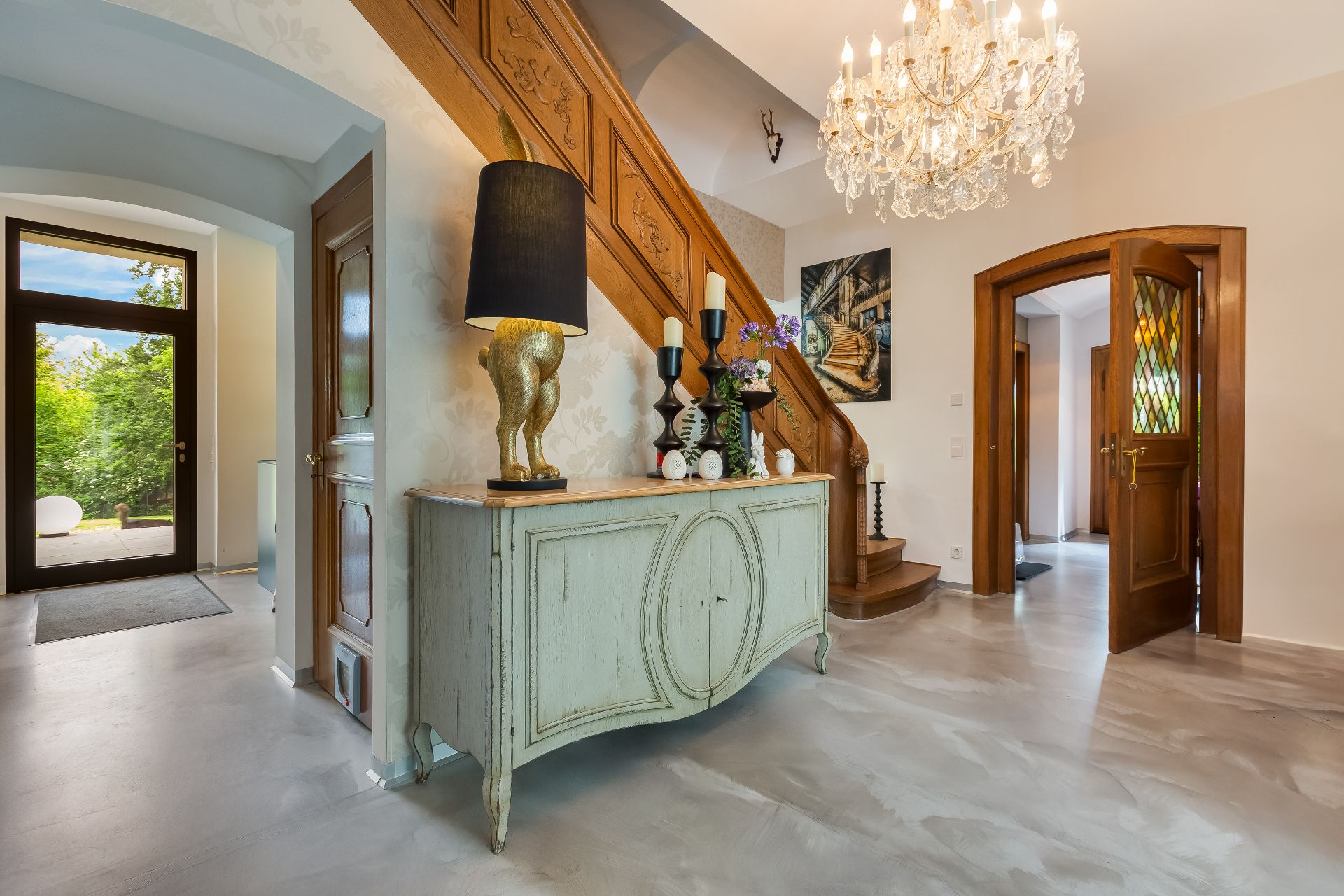 Heller Flur mit Holztreppe, Kronleuchter und Kommode mit Dekoration.