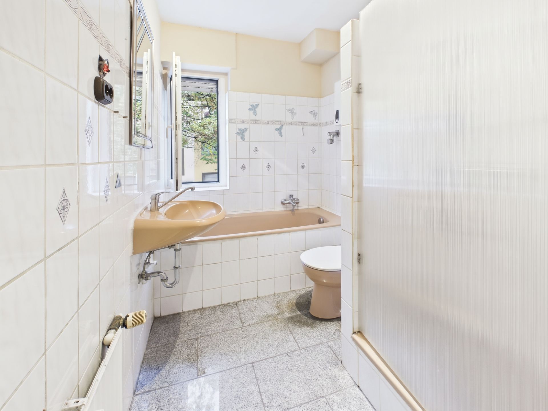 Helles Badezimmer mit brauner Badewanne, Waschbecken, Toilette und Fenster.