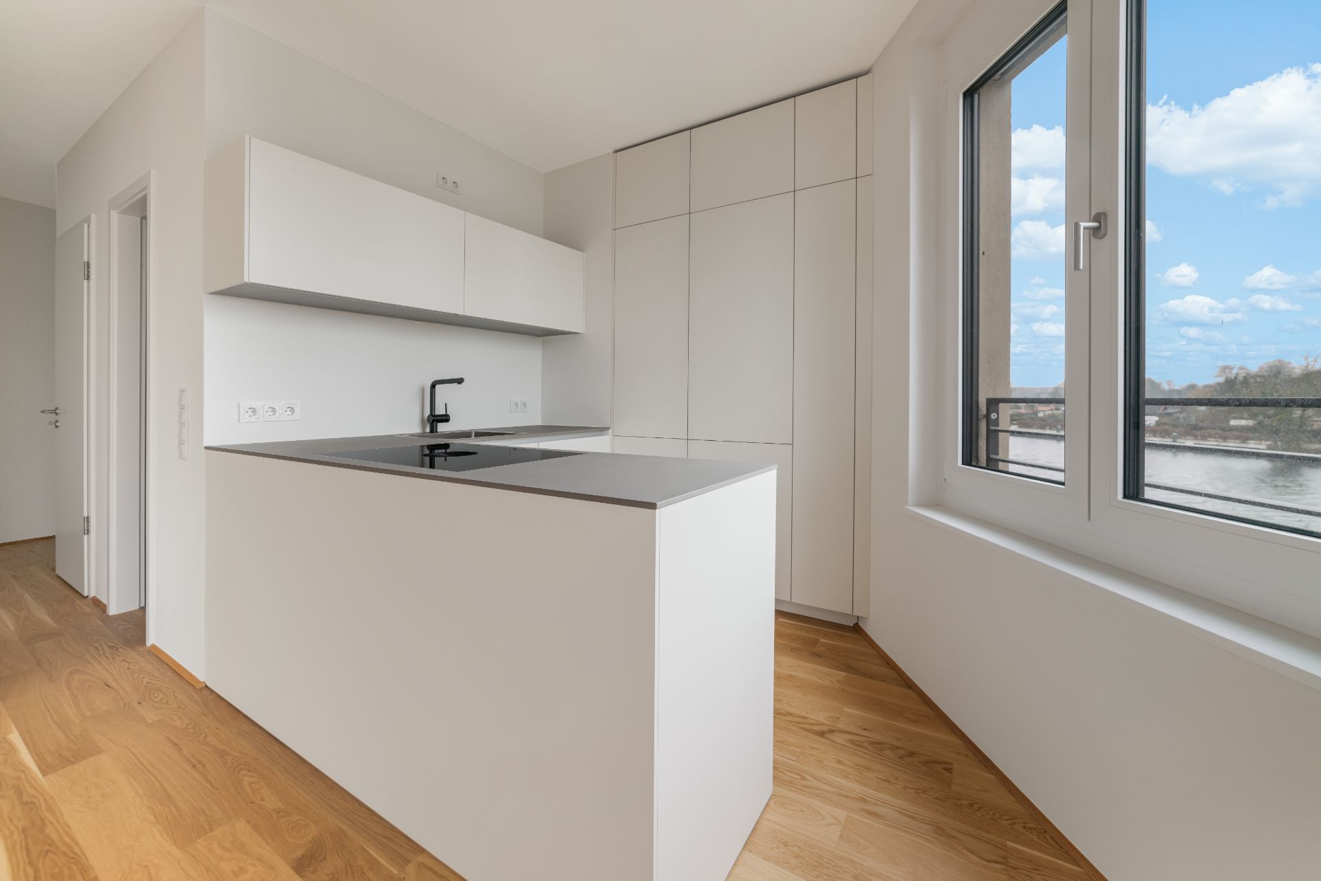 Moderne, helle Einbauküche mit großen Fenstern und Blick nach draußen, Parkettboden.