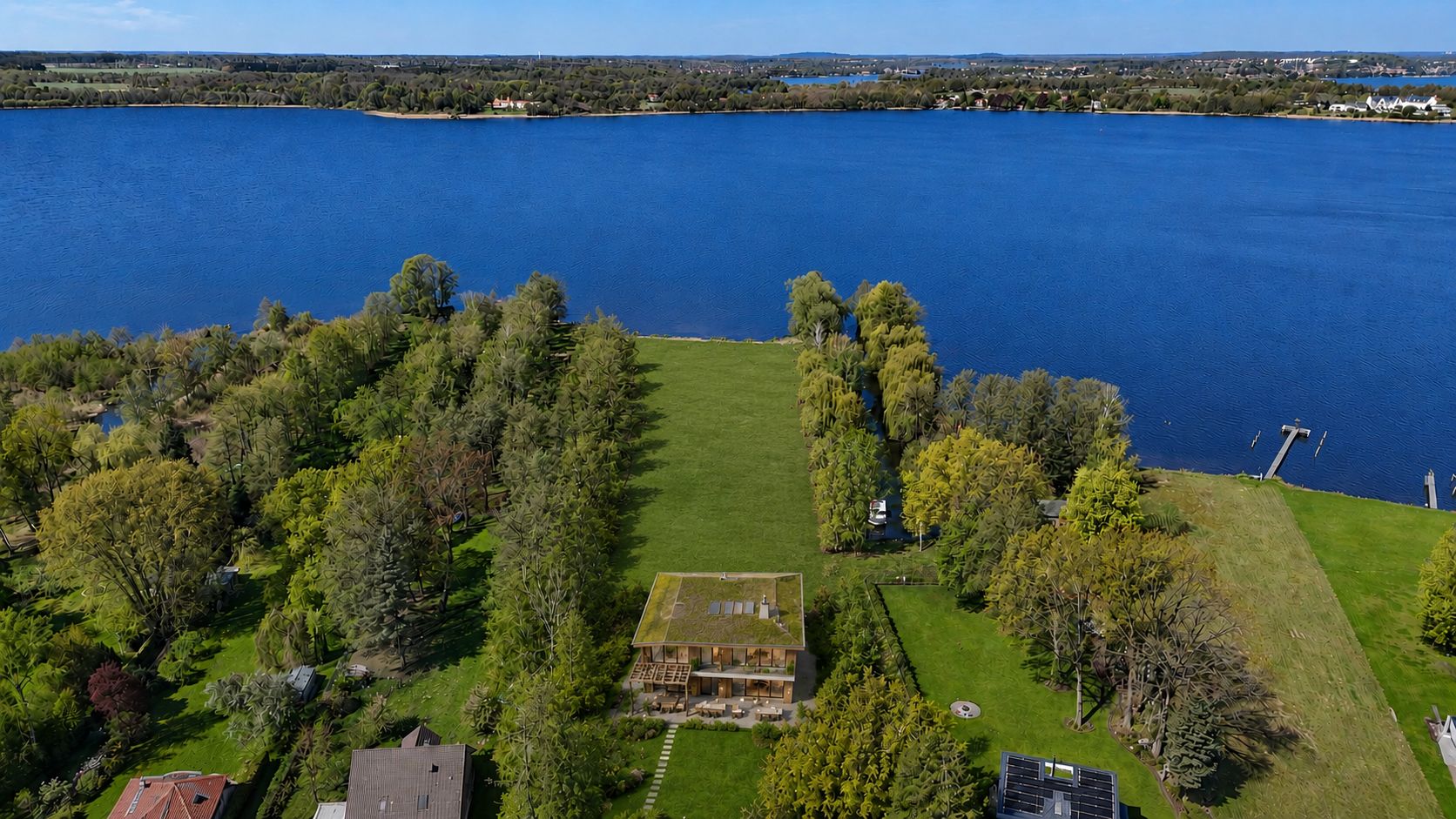 Luftaufnahme eines Hauses mit großem Garten direkt an einem See, umgeben von Bäumen.