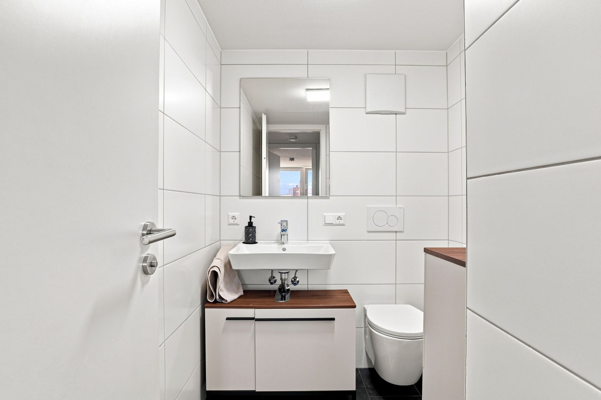 Modernes Bad mit Waschbecken, Spiegel, Handtuch und Toilette, weiße Fliesen an den Wänden.