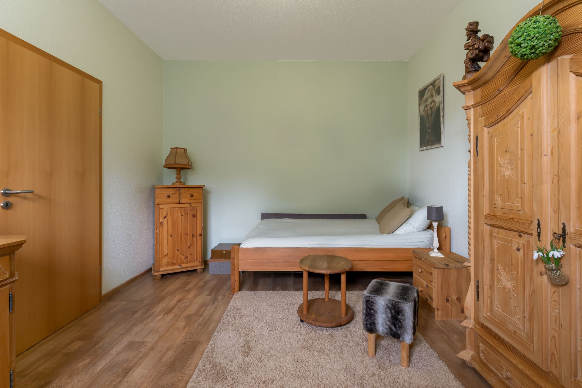 Schlafzimmer mit Holzbett, Schrank, Nachttisch, Kommode und Teppich auf Holzboden.