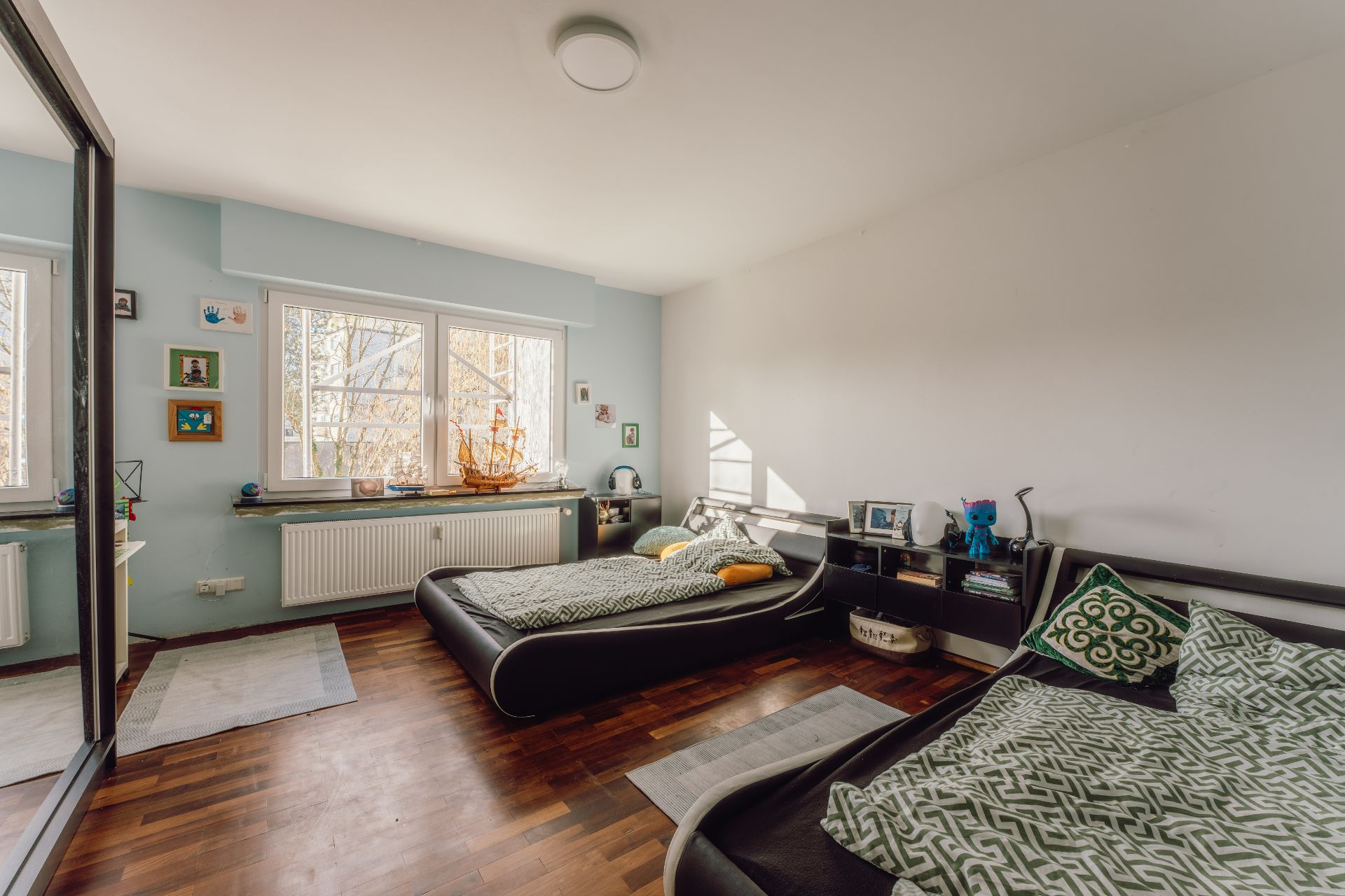 Helles Zimmer mit zwei Betten, Holzfußboden und großem Fenster, Regale und Dekoration sichtbat.