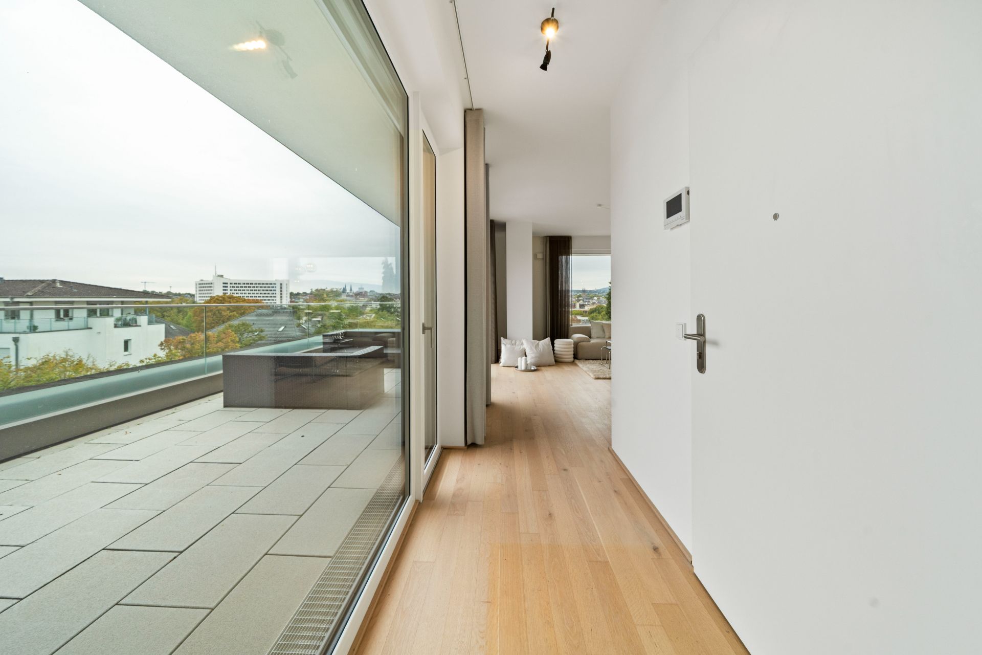 Heller Flur mit Holzboden, Zugang zu großer Terrasse mit Glasfront und Blick ins Freie.