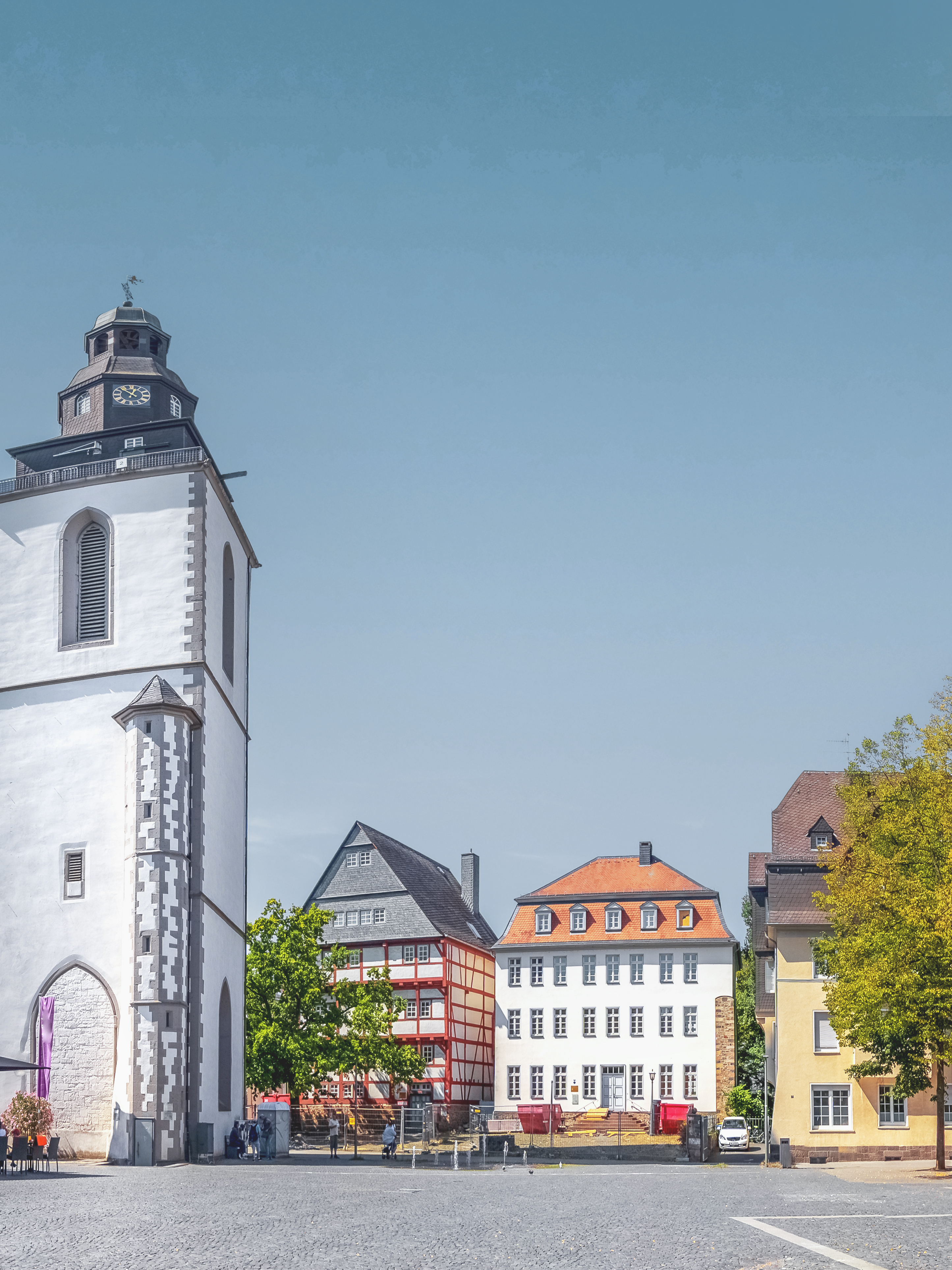 Historische Wohnhäuser und ein Kirchturm an einem Platz mit blauem Himmel.