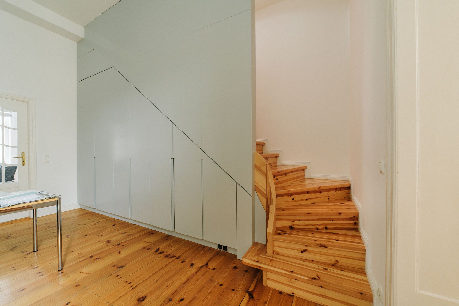 Holztreppe mit modernem Einbauschrank darunter in einem hellen Flur.