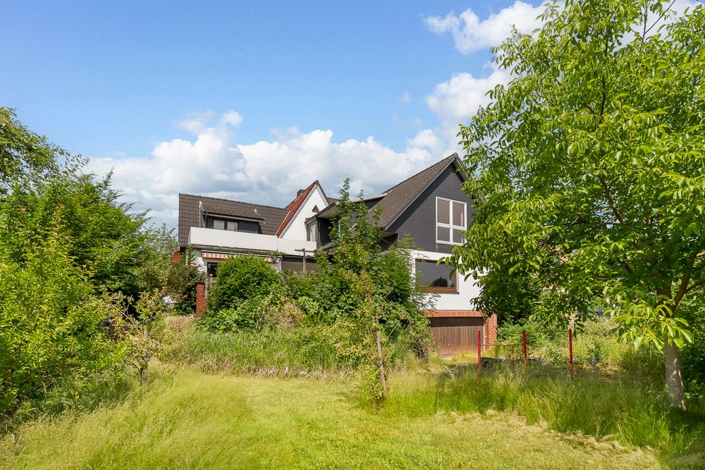Modernes Wohnhaus mit dunklem Dach und großem, grünem Garten im Vordergrund.