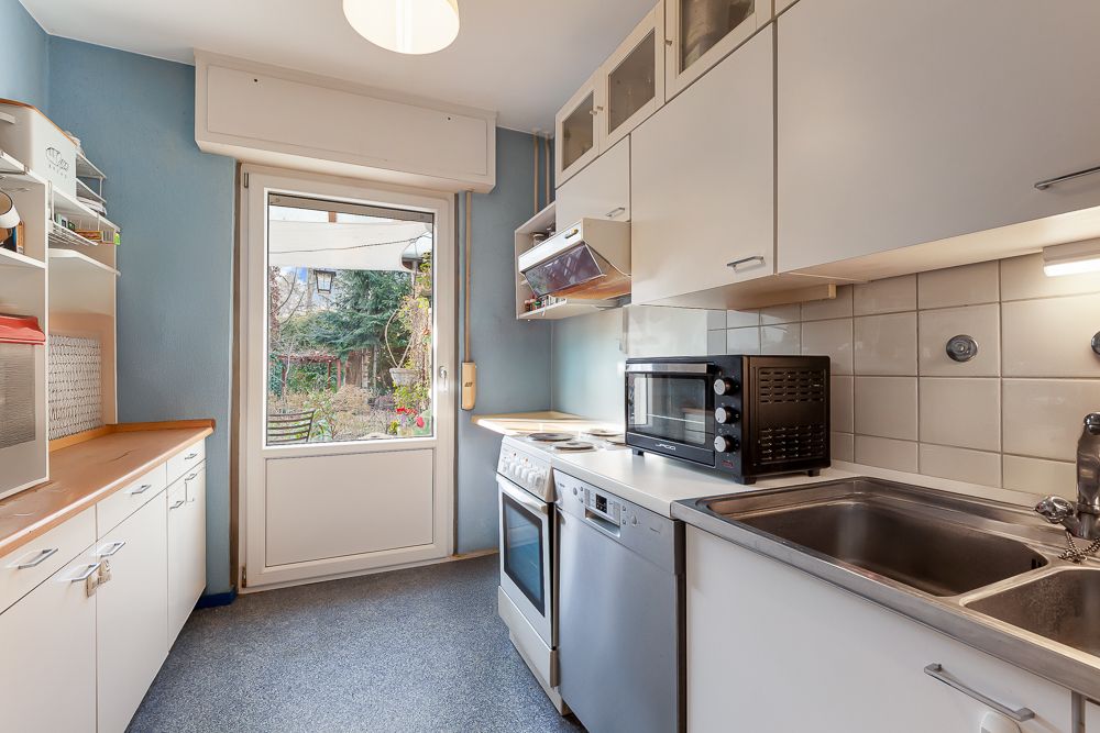 Moderne, helle Küche mit weißen Schränken, Herd, Spüle und Fenster zum Garten.