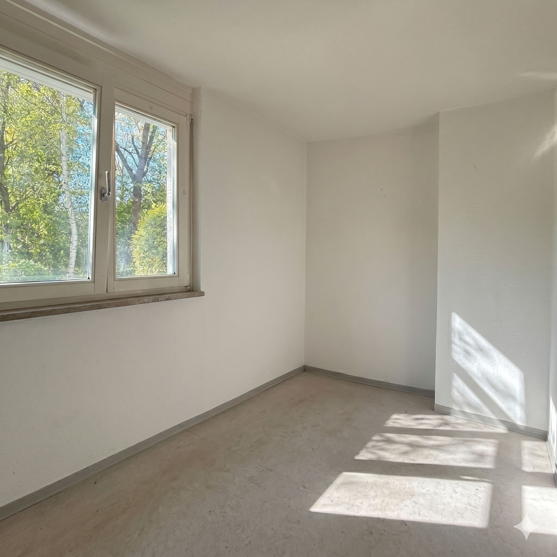 Heller leerer Raum mit großem Fenster und Blick ins Grüne.