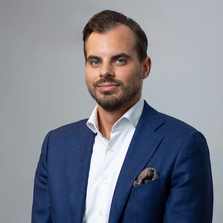 Ein Mann in blauem Anzug und weißem Hemd vor neutralem Hintergrund.