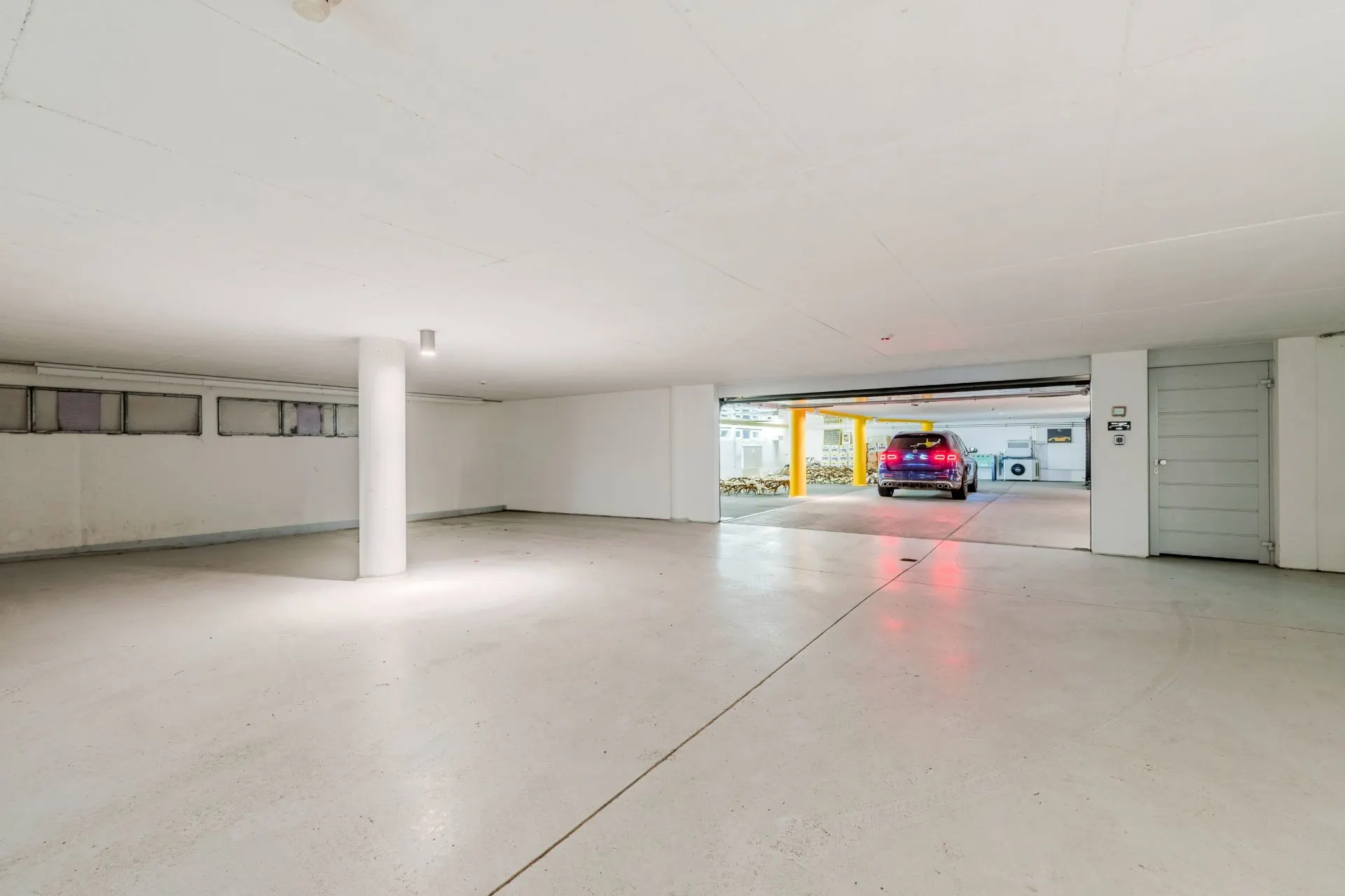 Helle Garage mit weißem Boden, einer Säule und einem geparkten Auto im Hintergrund.