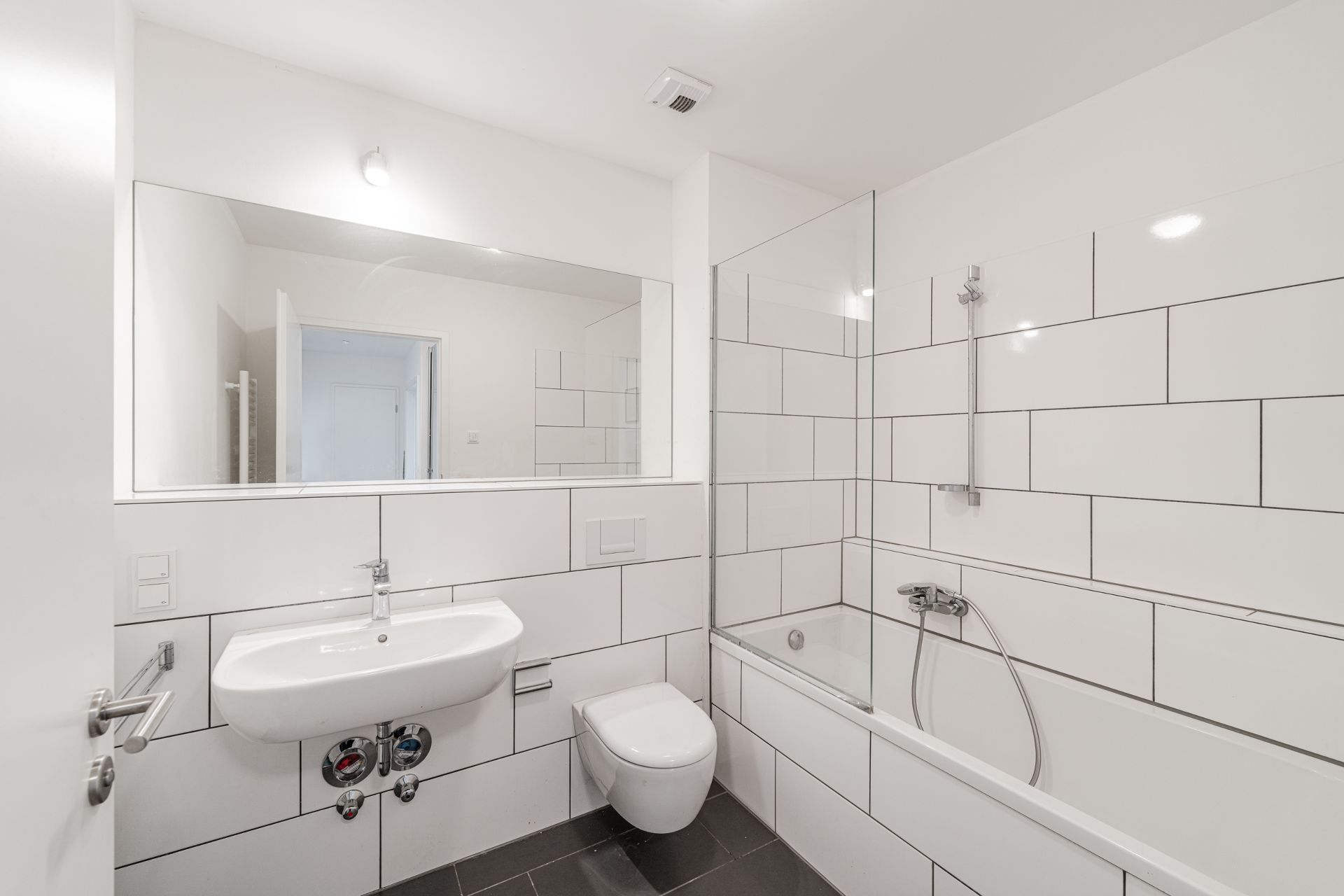 Modernes Badezimmer mit weißer Badewanne, Waschbecken, WC und großem Spiegel.