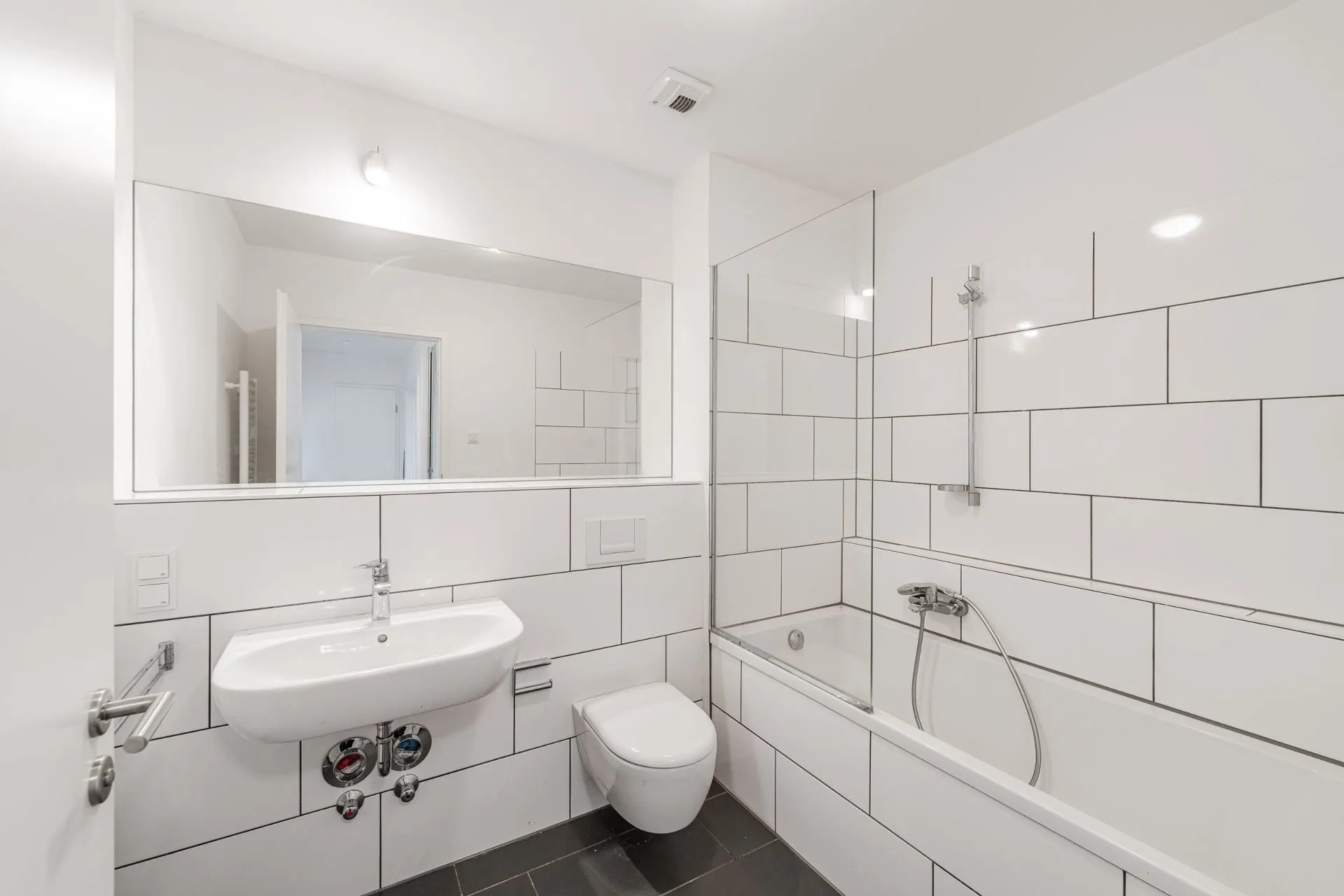 Modernes Badezimmer mit weißer Badewanne, Waschbecken, WC und großem Spiegel.