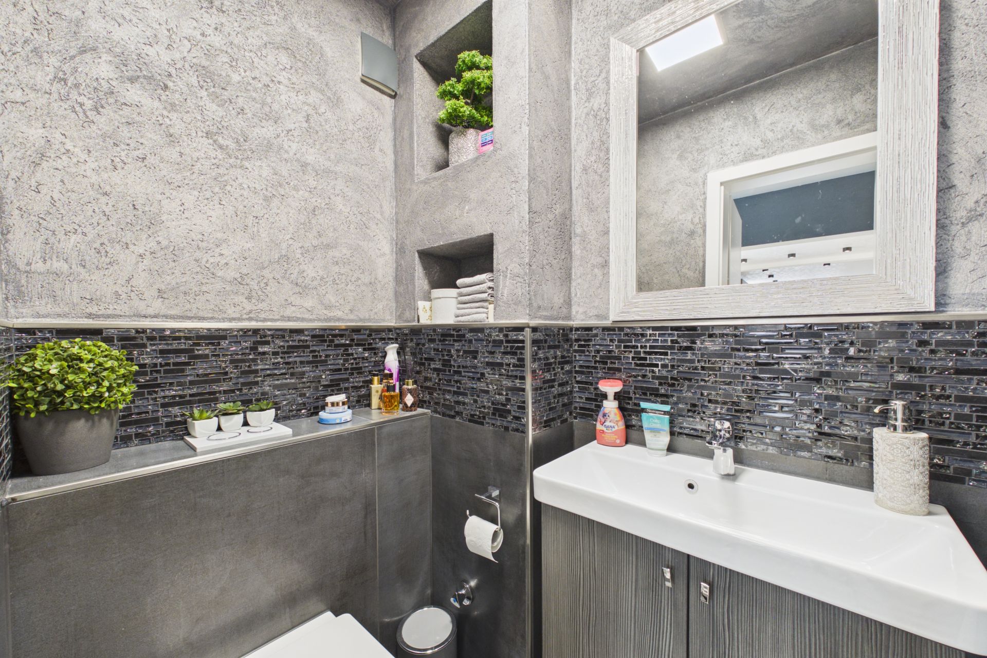Modernes Badezimmer mit Waschbecken, Spiegel, Toilette, Pflanzen und Wandregalen.