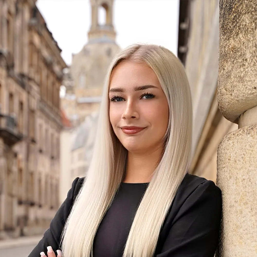 Frau mit langen, blonden Haaren steht draußen vor einem historischen Gebäude.