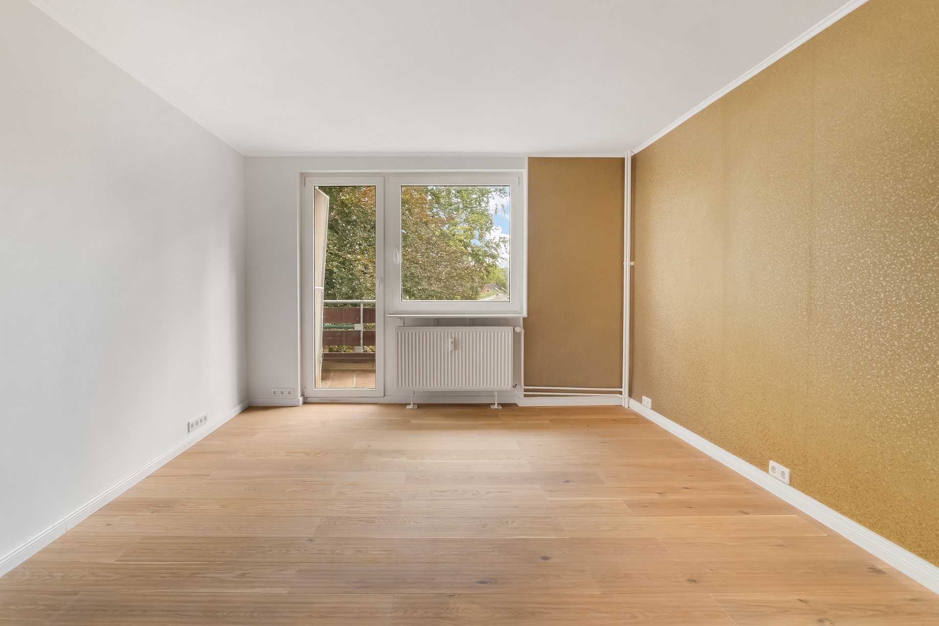 Leeres Zimmer mit Holzfußboden, gelber Wand und Fenster mit Tür zum Balkon.
