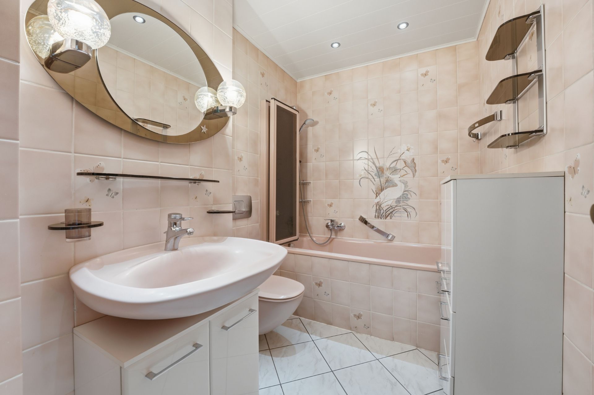 Badezimmer mit rosa Fliesen, Waschbecken, Badewanne, WC und Wandspiegel.