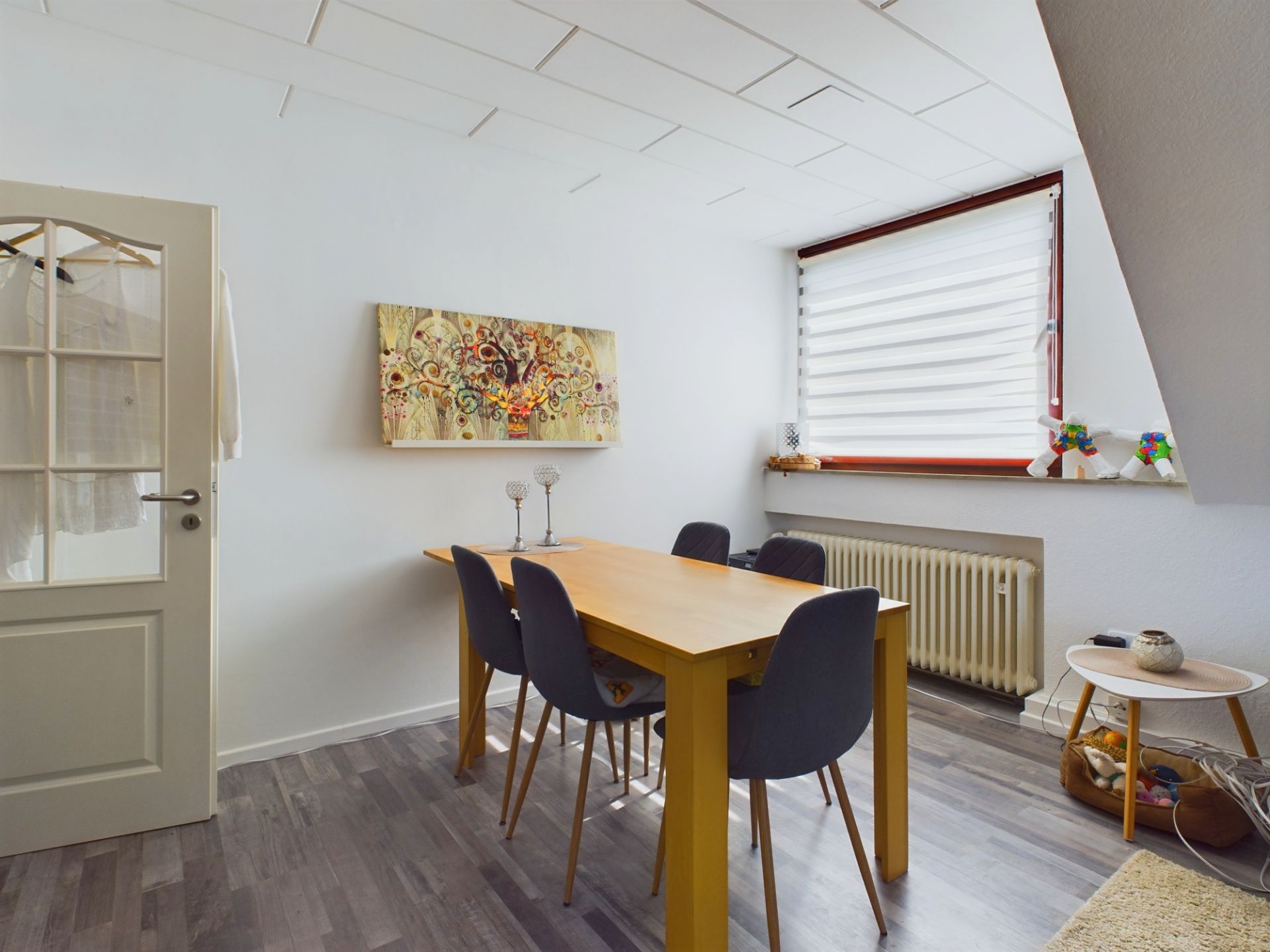 Esszimmer mit Holztisch, vier Stühlen, großem Fenster und bunter Wandkunst.