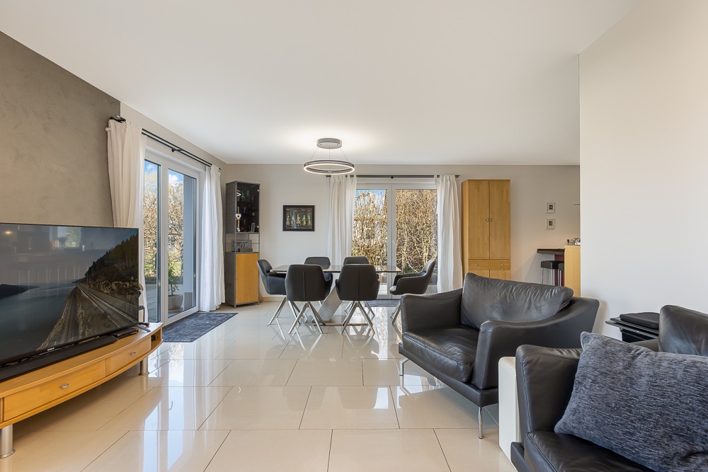 Modernes Wohnzimmer mit Ledersofas, Fernseher, Esstisch und großen Fenstern.