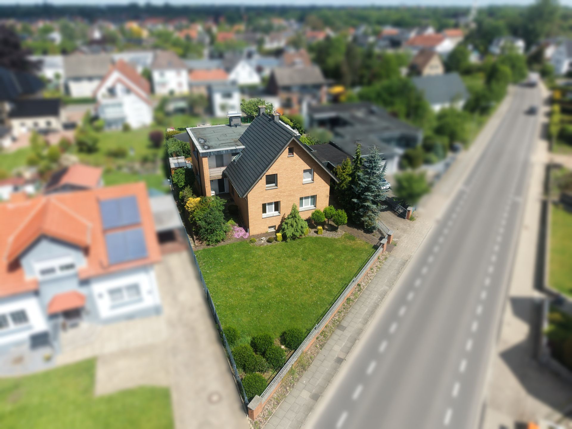 Luftaufnahme eines Einfamilienhauses mit großem Garten an einer Straße.