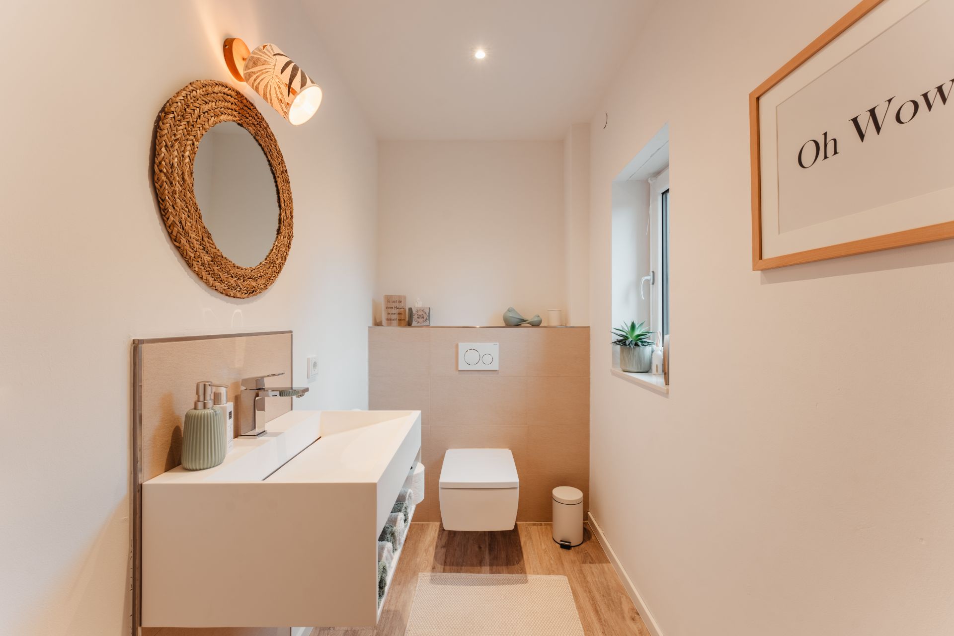 Modernes, helles Badezimmer mit rundem Spiegel, Waschbecken, Toilette und Fenster.