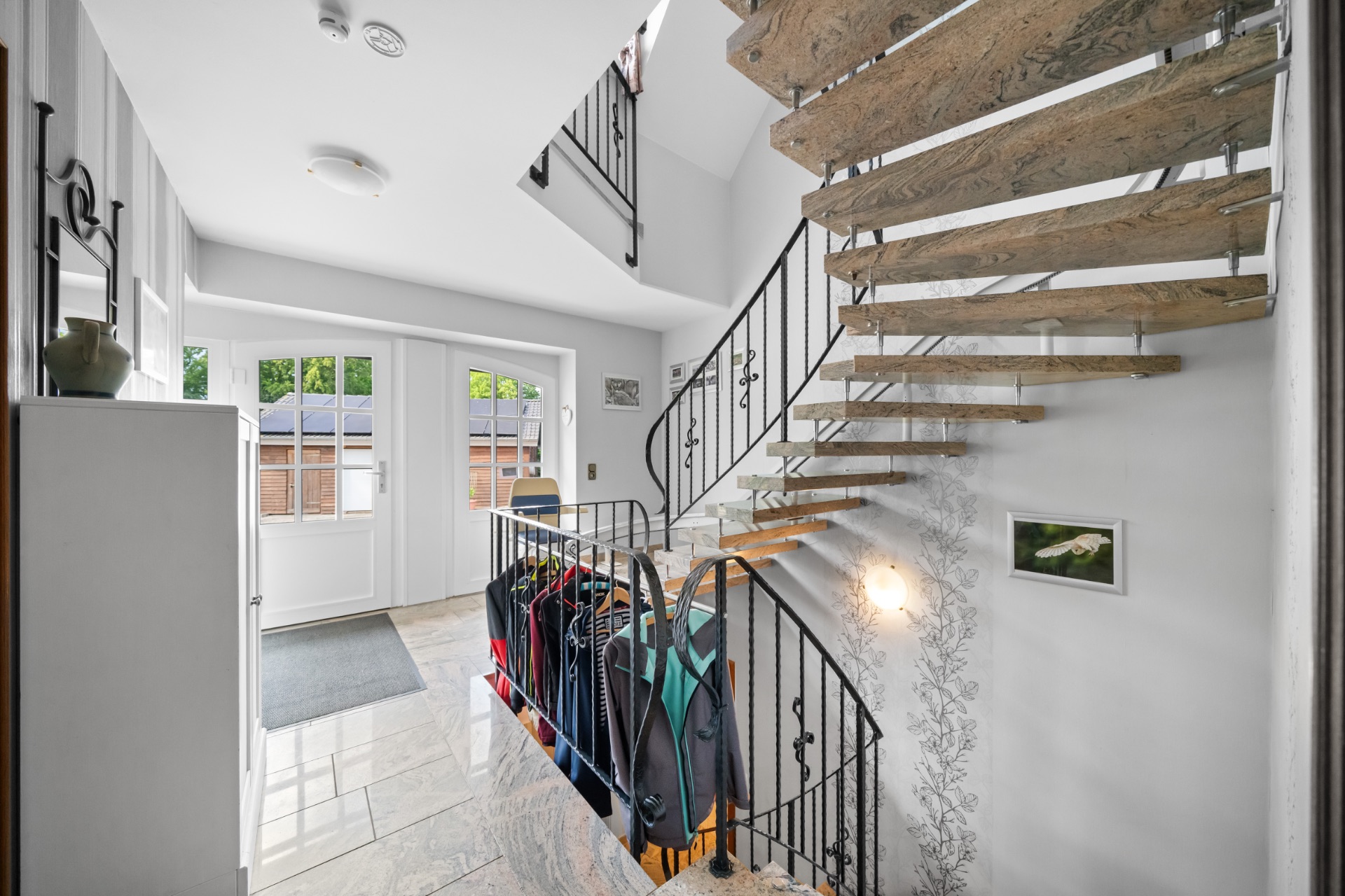 Heller Flur mit offener Holztreppe, Kleiderschrank und Fensterblick nach draußen.