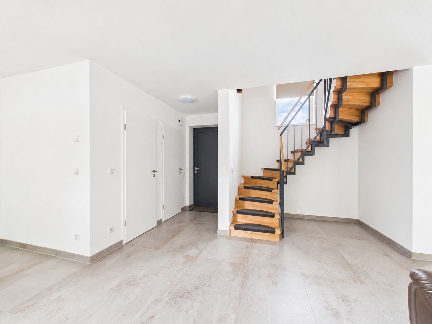 Heller Flur mit Holztreppe, weißen Wänden und mehreren geschlossenen Türen.