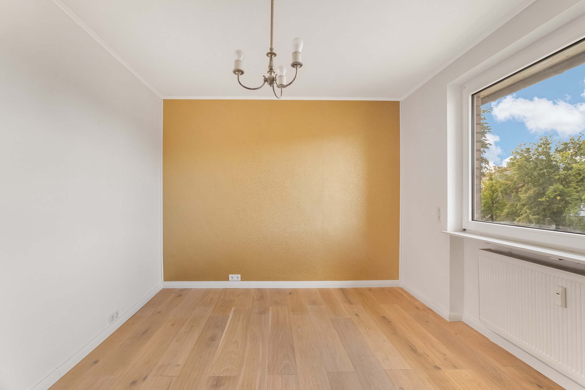 Leeres Zimmer mit goldfarbener Wand, Holzfußboden, Fenster und Deckenlampe.