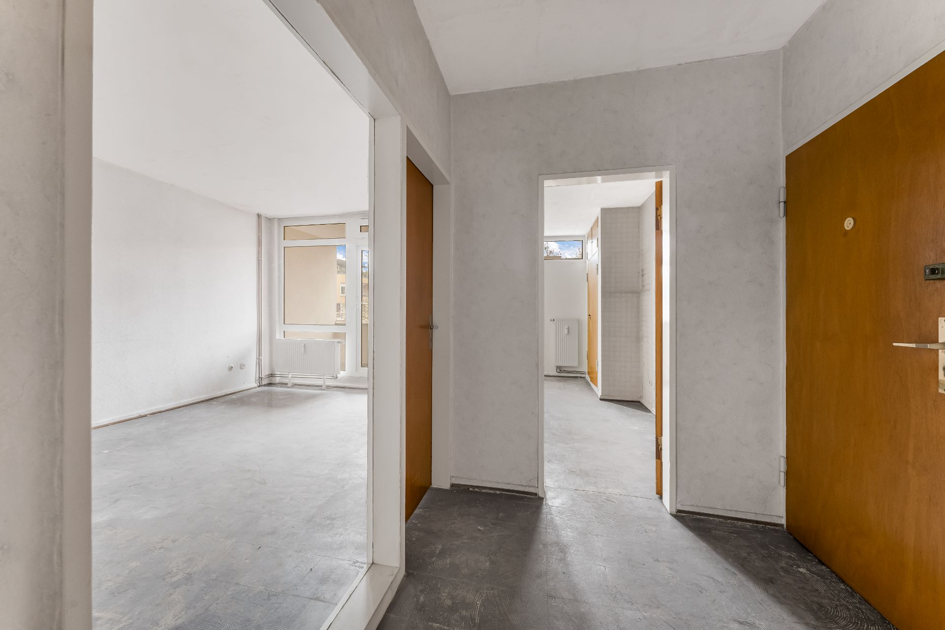 Leerer Flur mit Blick in ein helles Zimmer und offene Türen zu weiteren Räumen.
