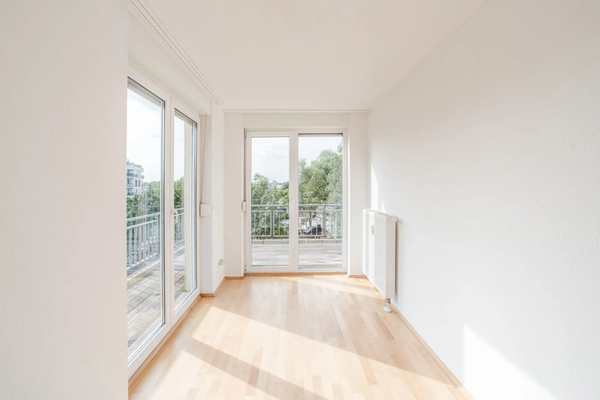 Heller Raum mit Parkettboden, großen Fenstern und Zugang zu einem Balkon.