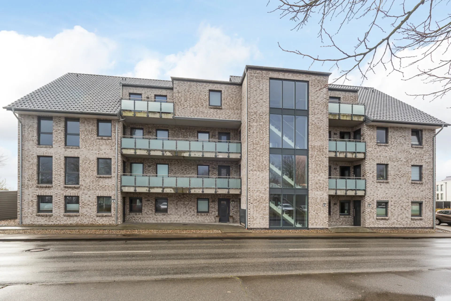 Modernes Mehrfamilienhaus mit Balkonen und großem Treppenhaus mit Glasfront.