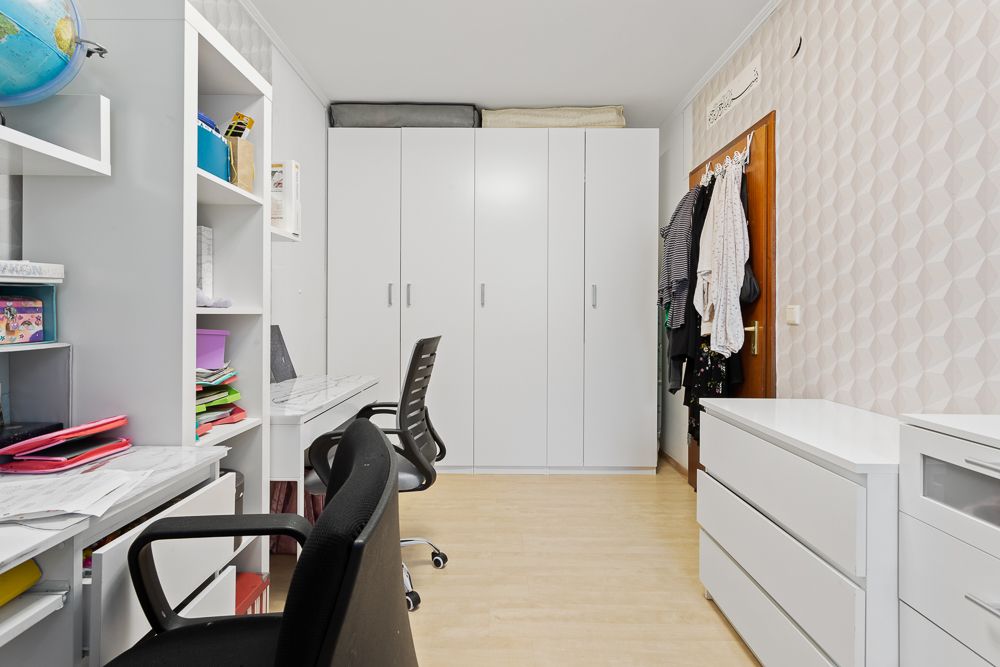 Helles Arbeitszimmer mit weißen Schränken, Schreibtischen und Regalen, zwei Stühlen und Kleidung an der Tür.