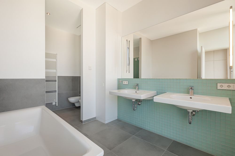 Modernes Bad mit Badewanne, zwei Waschbecken, Toilette und Handtuchheizkörper.