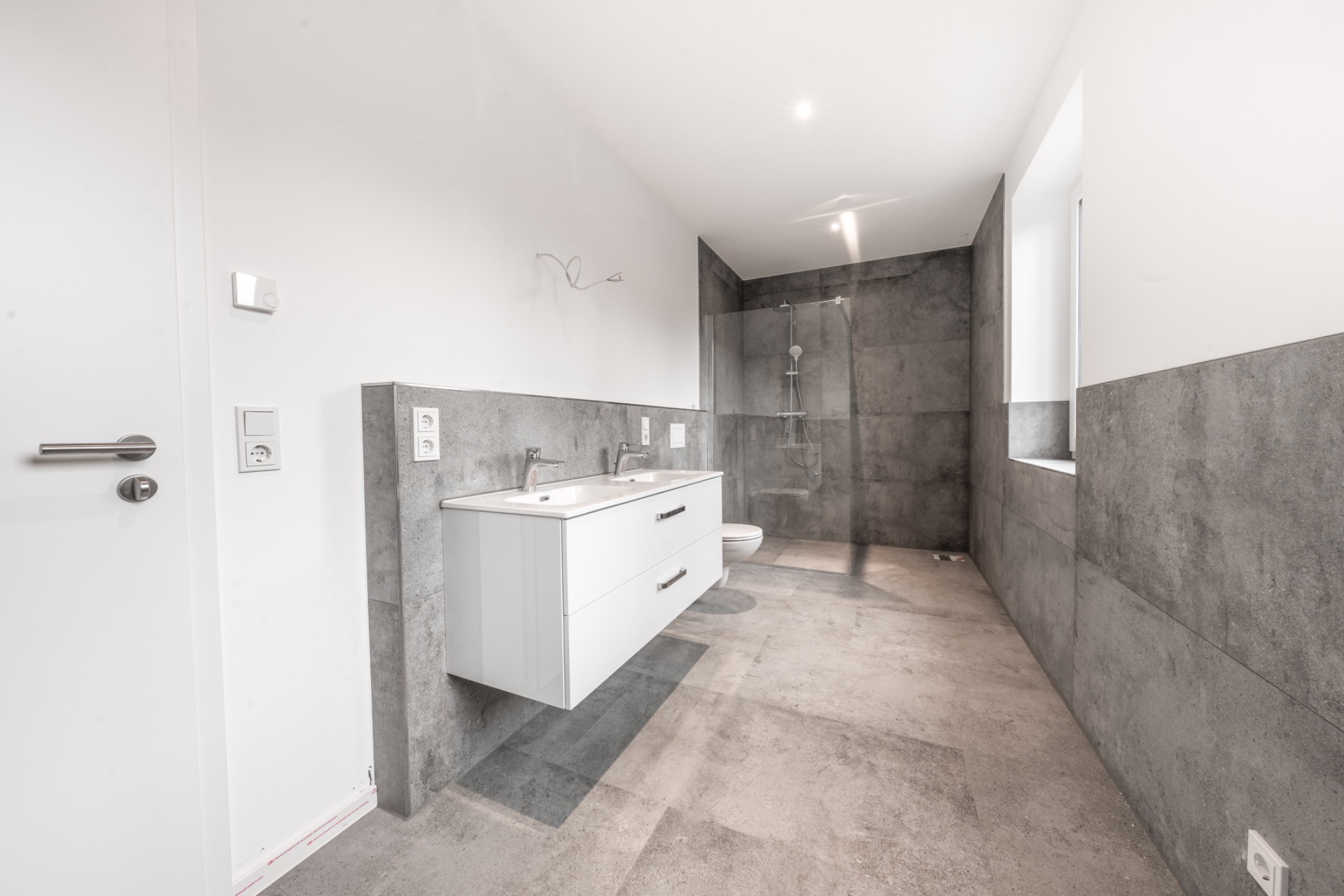 Modernes Badezimmer mit Doppelwaschtisch, großer Dusche und grauen Fliesen.