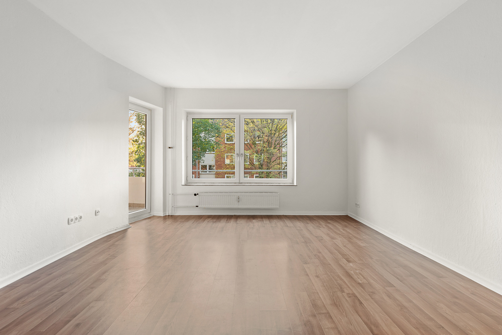 Helles, leeres Zimmer mit weißem Wänden, Holzfußboden und großem Fenster.