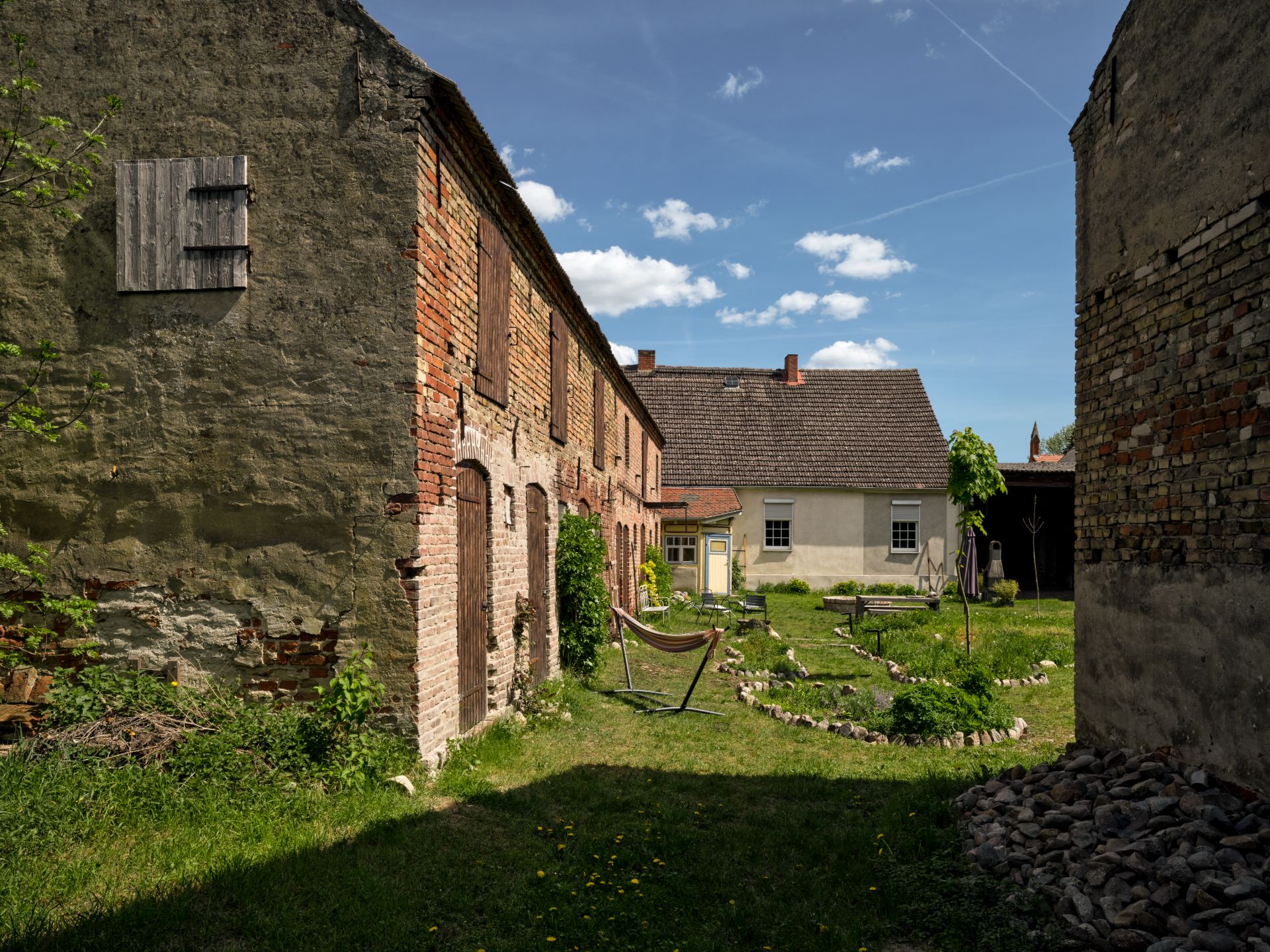 Innenhof mit alten Ziegelgebäuden, Rasenfläche, Steinkreisen und einer Hängematte.